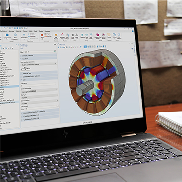 A laptop computer showing the COMSOL Multiphysics UI with an electric motor model in the Graphics window.