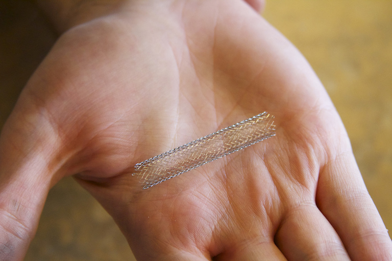 A photograph of a stent held in a human hand.