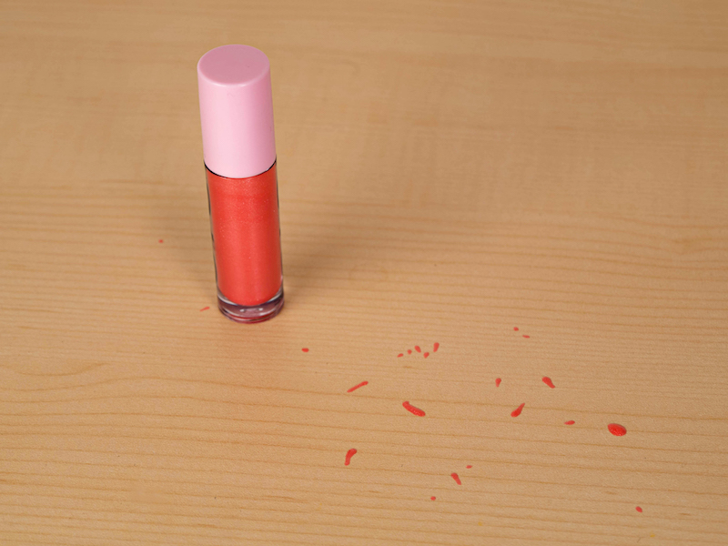 A photograph of lip gloss where some of the gloss spilled onto the table.