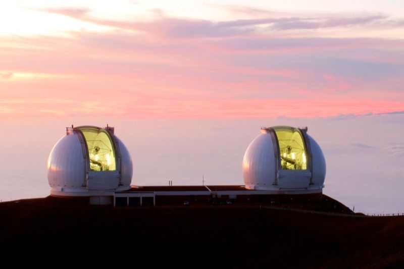 在粉红色和紫色日落的背景下拍摄的两台凯克望远镜的照片