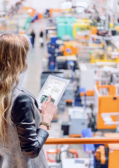 Female manager overseeing a factory while holding a tablet with a simulation app on the screen.