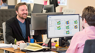 Two male colleagues sitting at their desks in an open-floor-plan-style office with simulations showing on one of their desktop monitors.