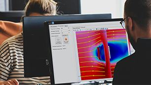 A female and male colleague sitting at their desks in an office with a simulation showing on one of their desktop monitors.