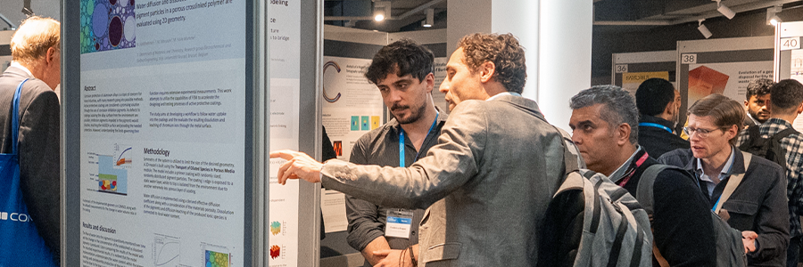 COMSOL Conference attendees discussing a poster in the exhibition hall.
