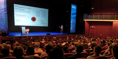 A keynote speaker presenting onstage to COMSOL Conference attendees.