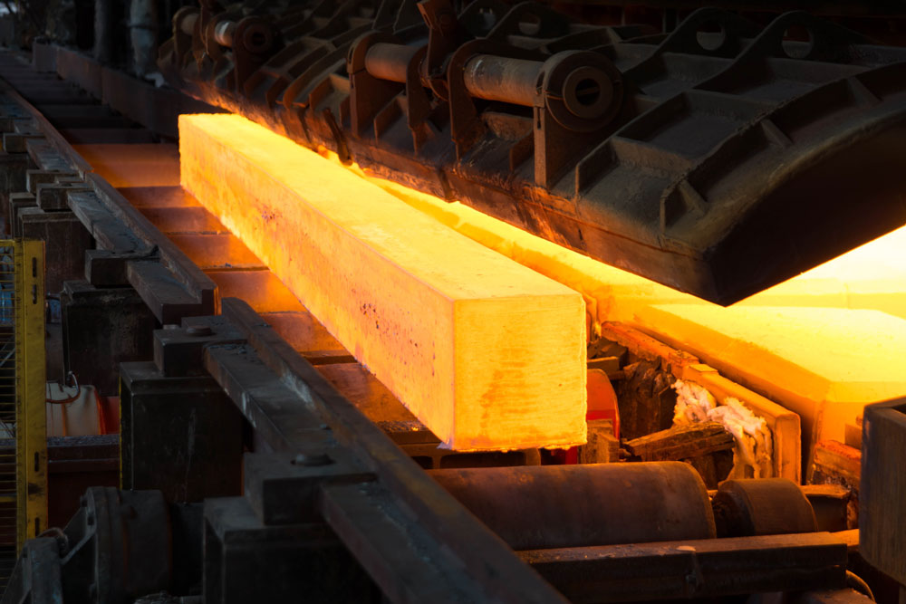 A photo of a glowing hot metal beam on a rolling rail in a manufacturing oven.