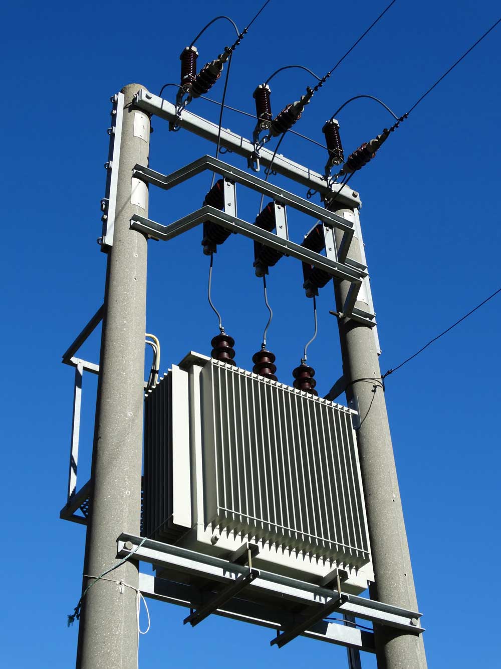 A photo from below of a transformer and power lines with a blue sky in the background.