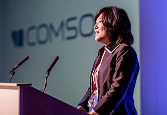 Five speakers sitting spaced apart onstage during a panel discussion; a slide containing an acoustics simulation is visible behind the speakers.