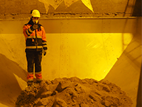 A man wearing a hardhat and uniform standing inside of a sand-filled heat storage vessel.