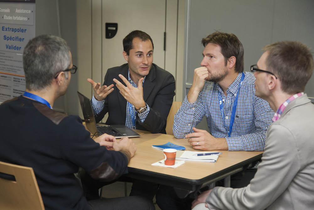 A photo of COMSOL Conference attendees discussing multiphysics simulation.