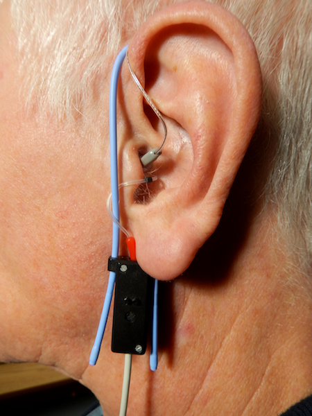 A photograph of a probe tube microphone hanging from a human ear.