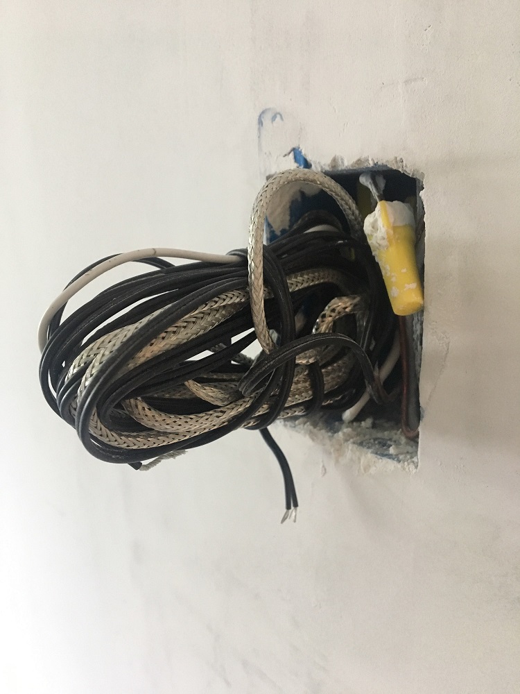 A photograph of a roll of electrical cables coming out of a wall.