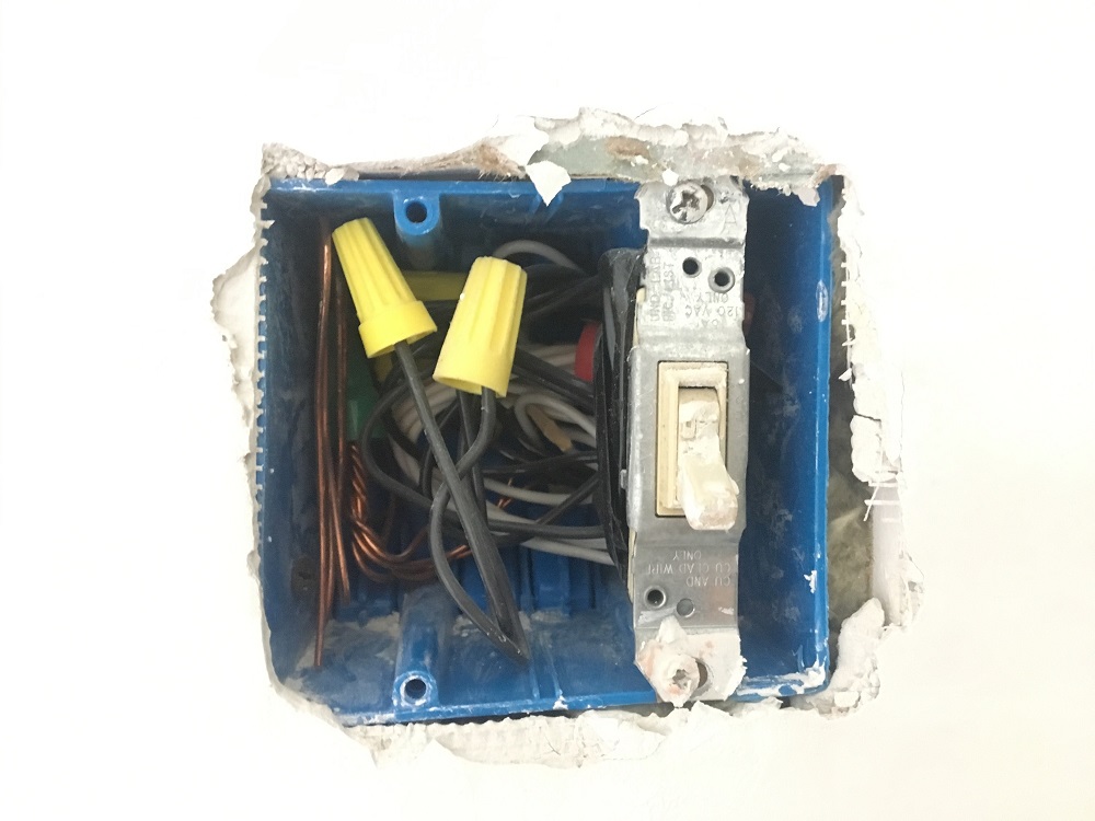 A photograph of wires behind an electrical light switch.
