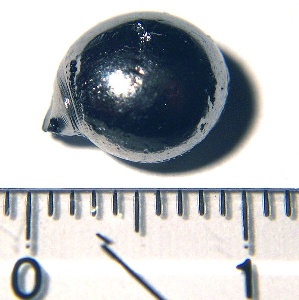 A photograph of a small pellet of rhenium next to a ruler for scale.