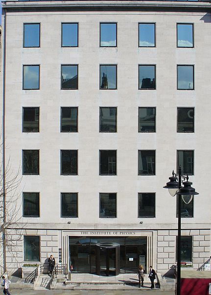 The façade of a nondescript gray building with 27 windows and a wide entrance.