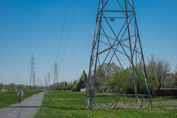 A photograph of transmission lines going down a country road with a bicyclist on the side.