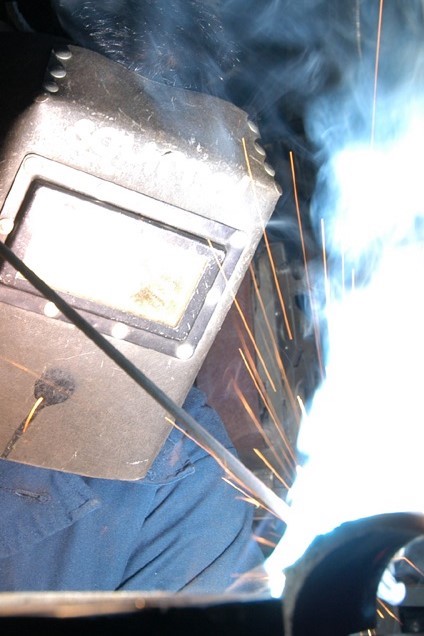 A photograph of an arc welder wearing a mask as sparks fly up from the machinery.