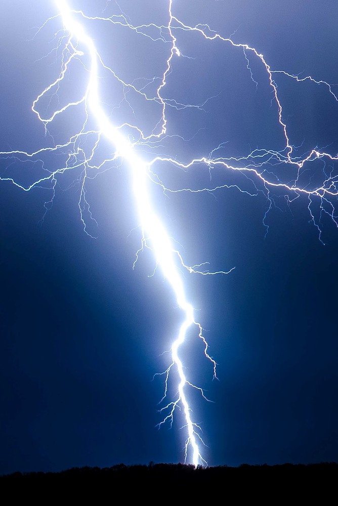 A photograph of a lightning bolt against the backdrop of a dark blue sky.