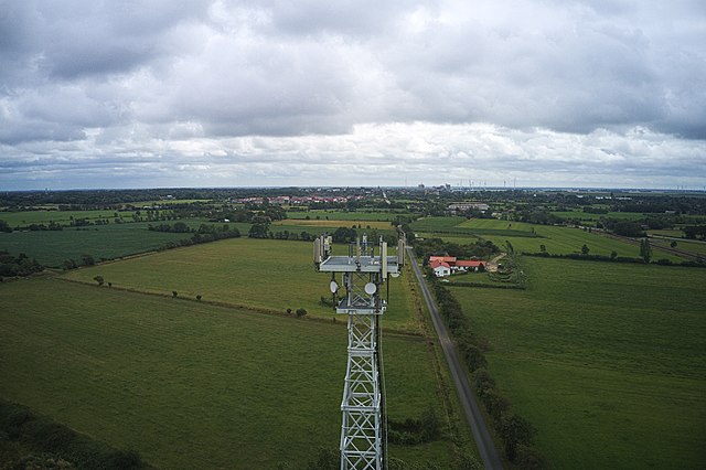 Photographie aérienne d'une tour de communication 5G entourée de champs agricoles.