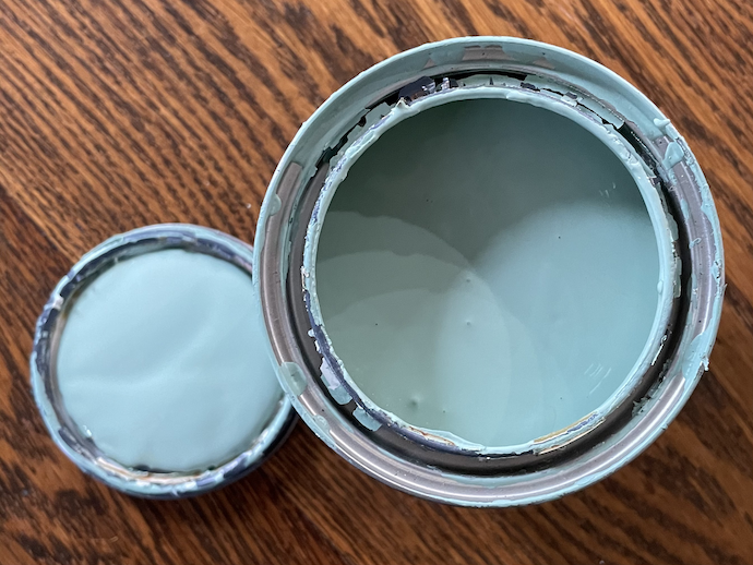 A photograph of a can of blue paint and its lid on a wooden table.