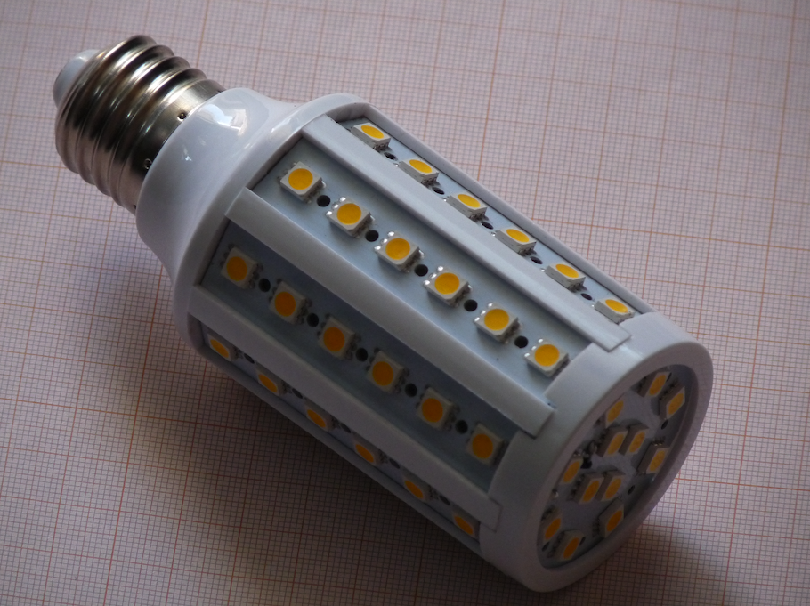 A photograph of a white LED corn bulb with yellow LED chips, resting on a piece of gridded paper.