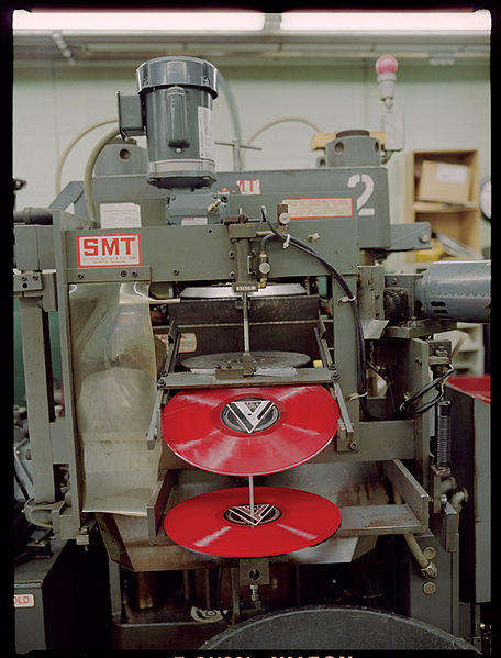 A photograph of a hydraulic press as it manufactures vinyl records in red.