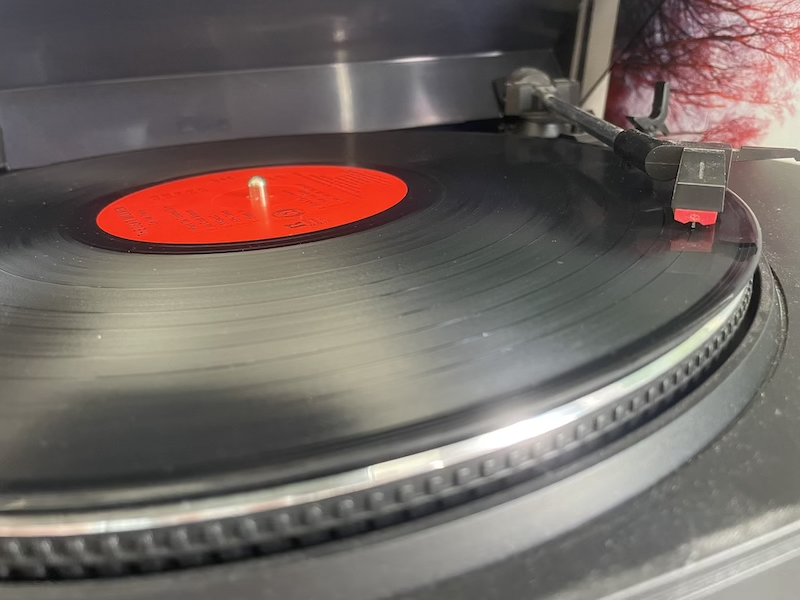 现代电唱机上带有红色标签的黑色黑胶唱片的照片，唱臂和唱针位于凹槽中。