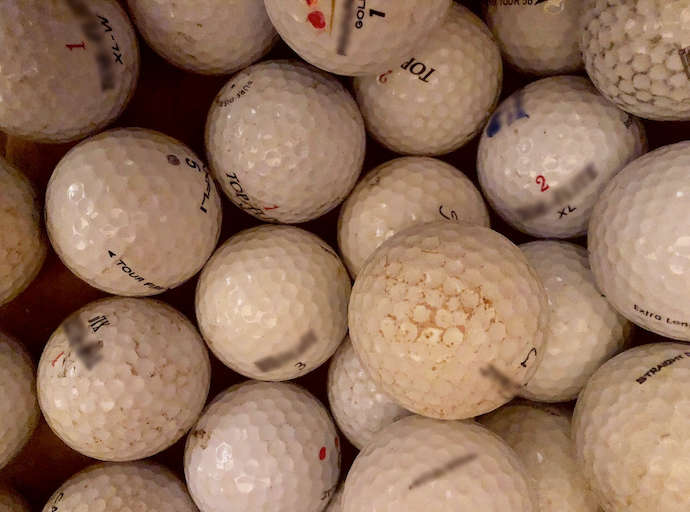Фотография кучи белых мячей для гольфа с лунками и потёртыми этикетками.