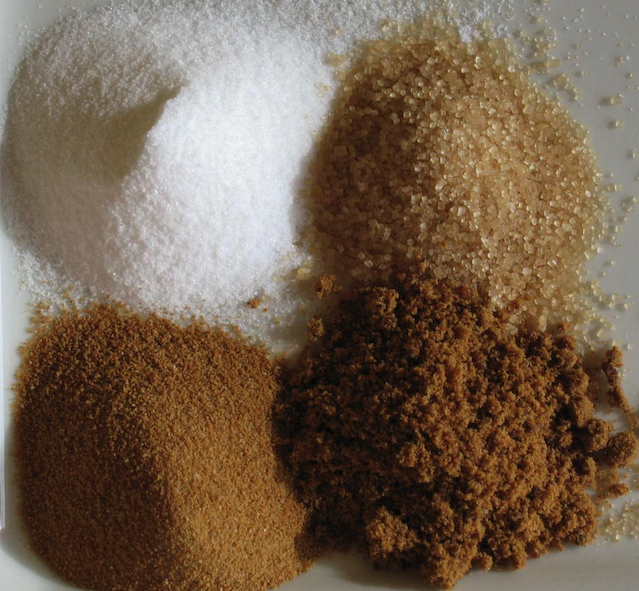 A closeup image of white refined, unrefined, brown, and unprocessed cane sugar (shown clockwise from top left).