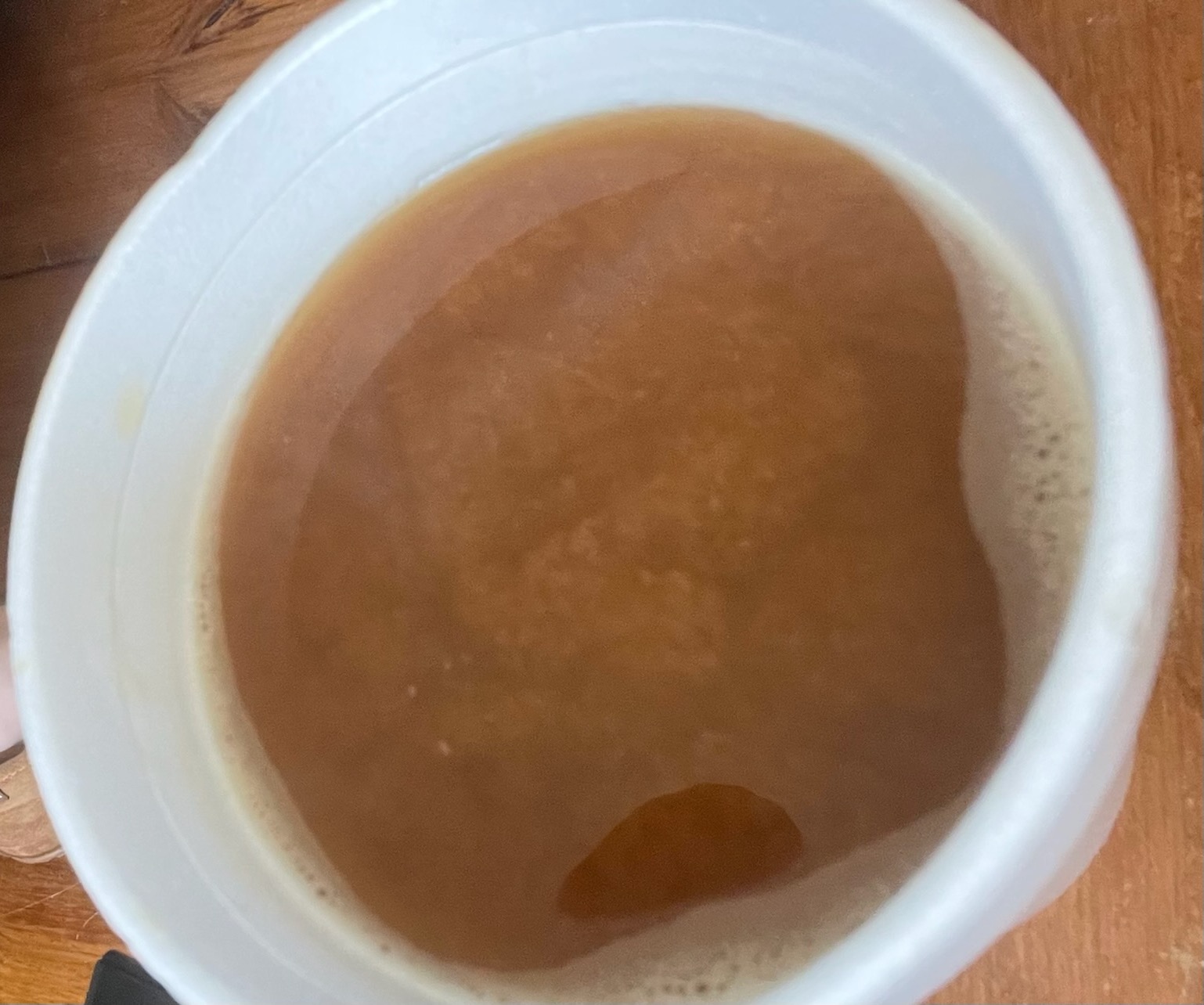 A close-up image of hot coffee and oat milk in a white coffee mug. The drink's surface appears grainy in texture.