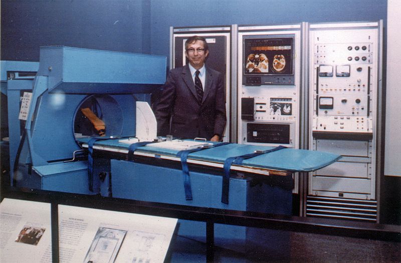 A photograph of Robert Ledley standing next to the first full-body CT scanner model.