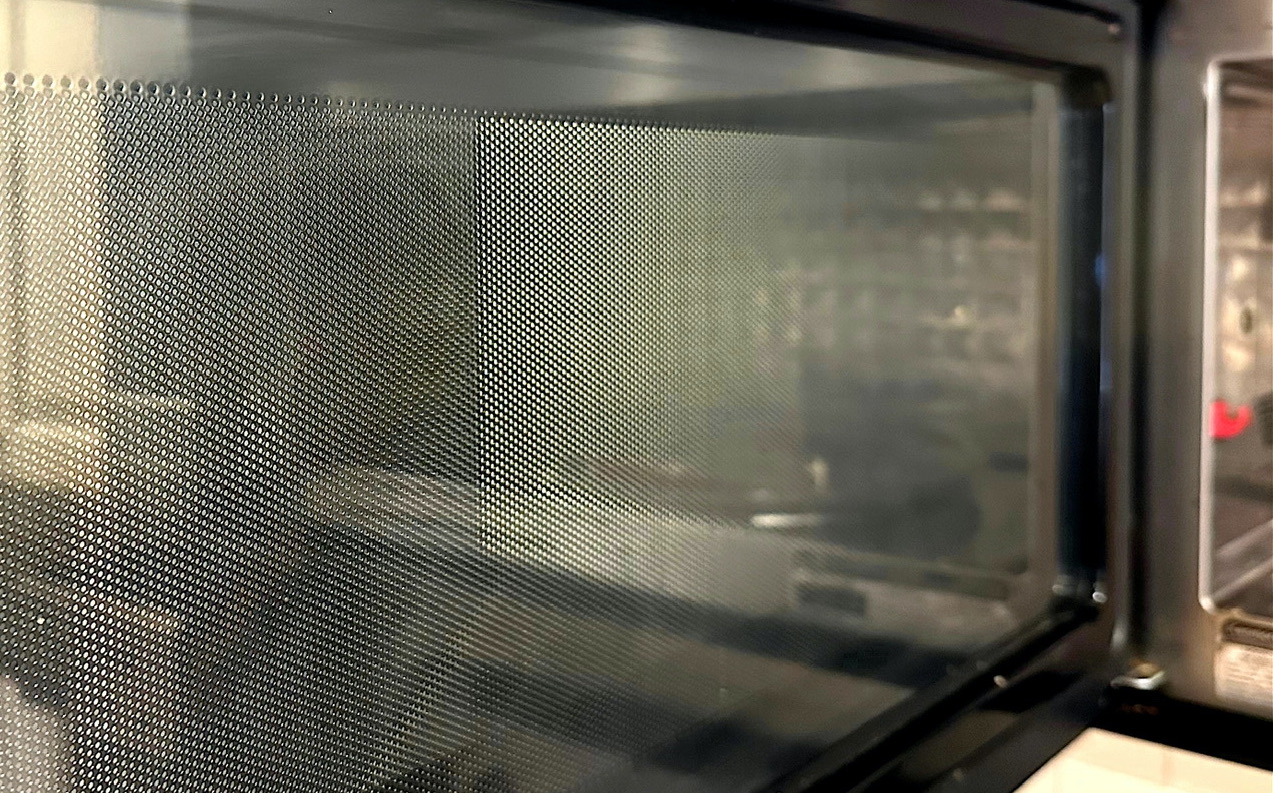 A close-up of the inside of a microwave's door, showing its grating.