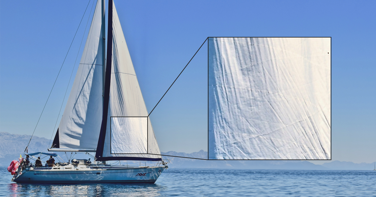 A wide shot image of a sailboat with a cut-out showing a zoomed-in view of wrinkles in the sail.
