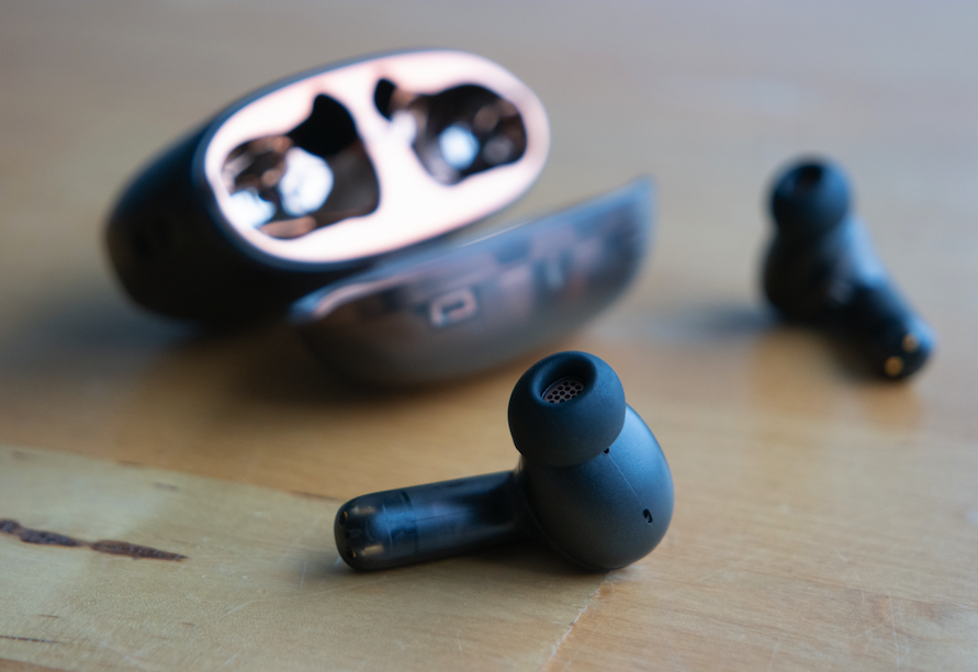 A close-up of headphones that feature MEMS drivers, shown laying on a wooden surface next to their open case.