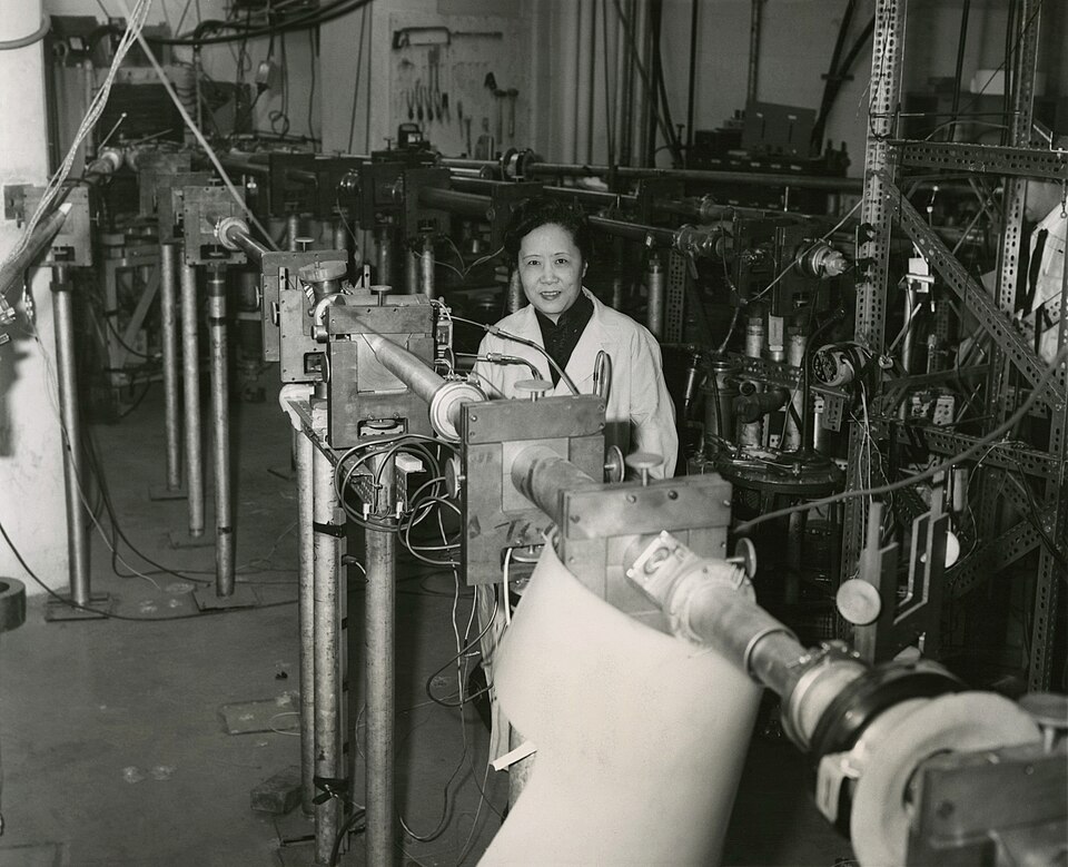 A black and white photograph of Chien-Shiung Wu standing in a laboratory surrounded by large equipment.