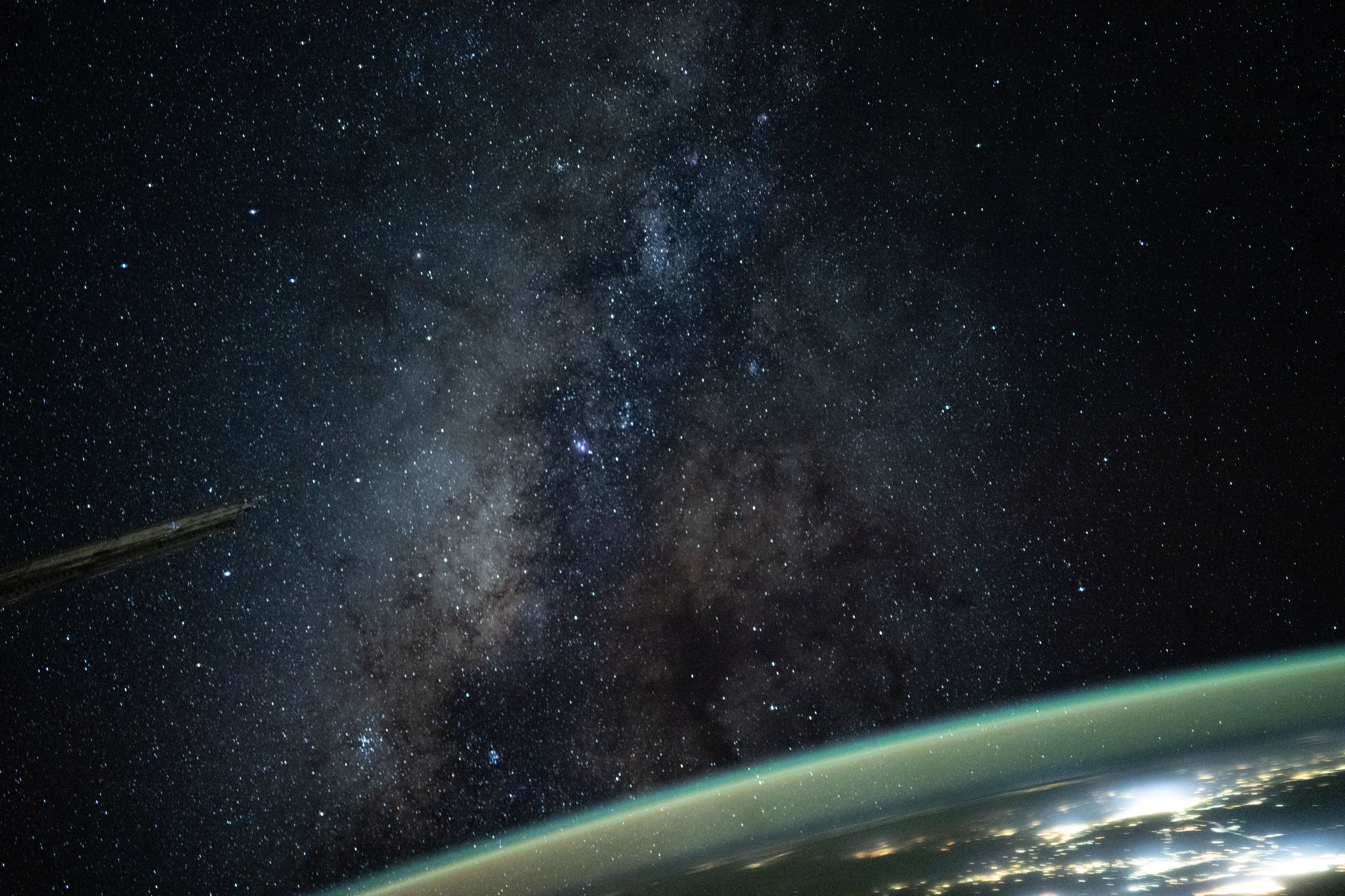 A color photograph of the Milky Way, with the black sky full of white pinpricks of stars and a green band on light across the bottom right corner.
